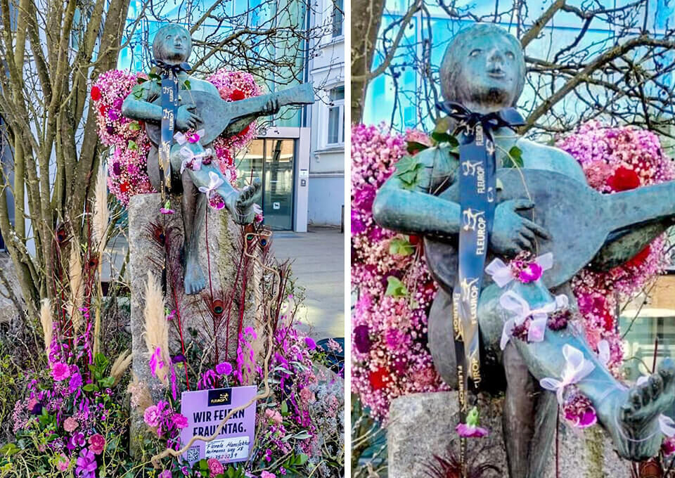 Gitarrenspielerin in Buxtehude blumig dekoriert zum Frauentag Statue der Gitarrenspielerin in Buxtehude, festlich mit pinkfarbenen Blumen, Schleifen und Blütenketten verziert zum Frauentag.