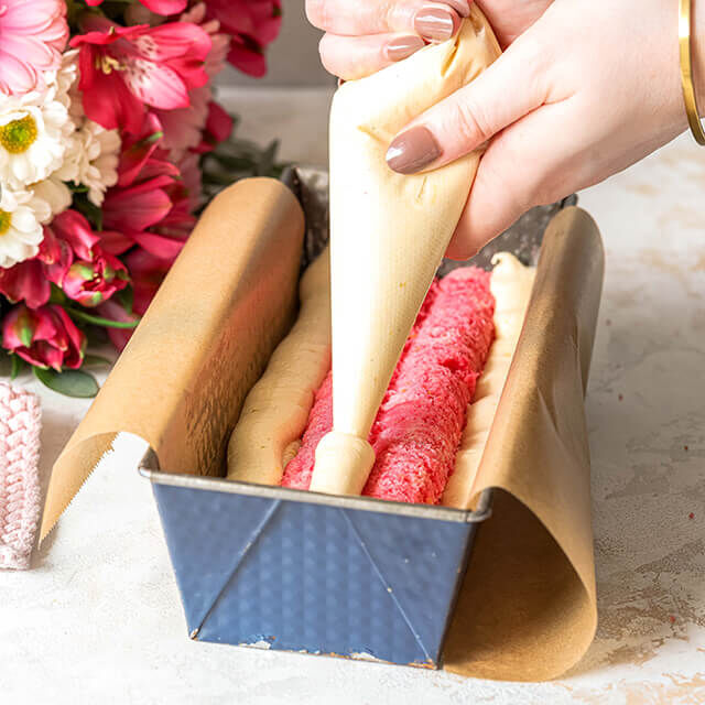 Herzkuchen Step 6 Mit einem Spritzbeutel wird heller Teig um die Herzstücke herum in die Kastenform gefüllt.