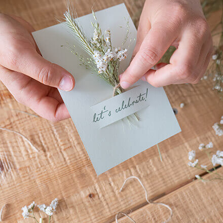 Ein Mini-Trockenblumenstrauß wird durch einen Schlitz in einer Hochzeitseinladungskarte gesteckt