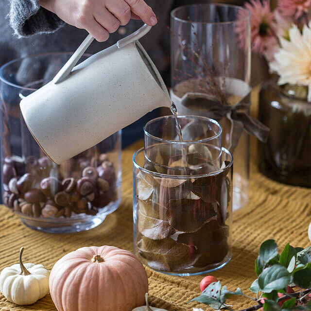 Glasvase mit Herbstlaub und Wasser für Dahlien vorbereiten