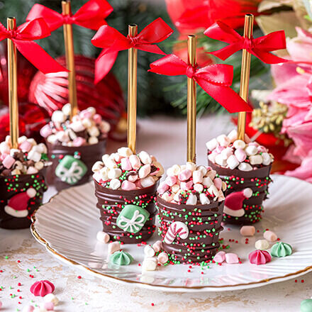 Fertige Hot Chocolate Bomb Cups auf einem Teller, dekoriert mit roten Schleifen und weihnachtlichen Akzenten.