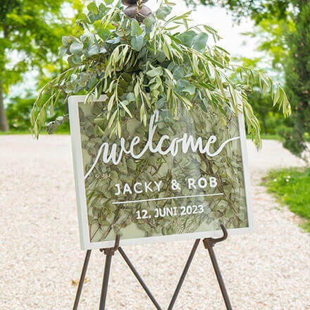Willkommenschild für eine Hochzeit, bestehend aus einem großen Bilderrahmen, welcher mit Eukalyptus befüllt und dekoriert ist und auf der eine Aufschrift steht