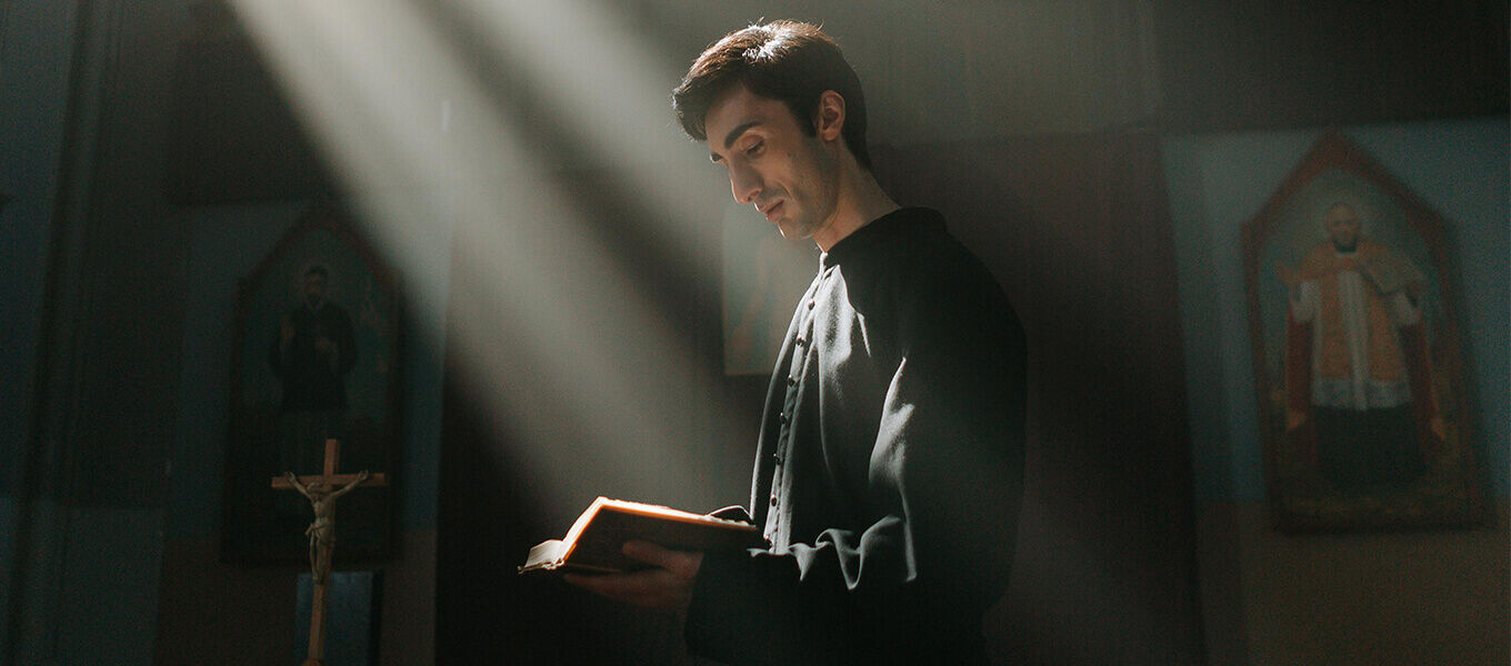 Junger Mann in einer Kirche liest aus der Bibel im Lichtstrahl – symbolisch für Konfirmation und Segen