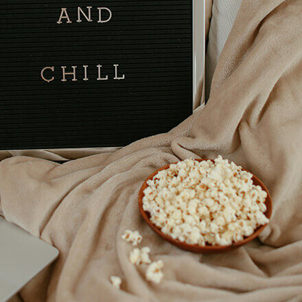 Eine Schale Popcorn steht auf einer beigen Decke neben einem Schild mit der Aufschrift "And Chill".