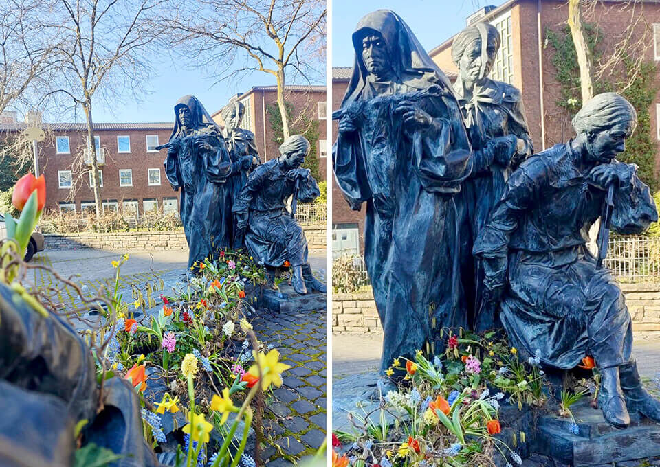 Edith-Stein-Denkmal in Köln mit Blumengestecken zum Frauentag Bronzestatue von Edith Stein in Köln, umgeben von frühlingshaften Blumenarrangements mit Tulpen und Narzissen zum Frauentag.