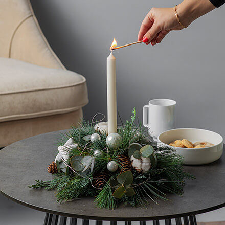 Kleines Adventsgesteck mit einer Kerze und klassischer Dekoration wie Tannenzweige und Kugeln.