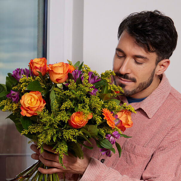 Mann riecht an einem bunten Blumenstrauß als Geschenk zum Geburtstag