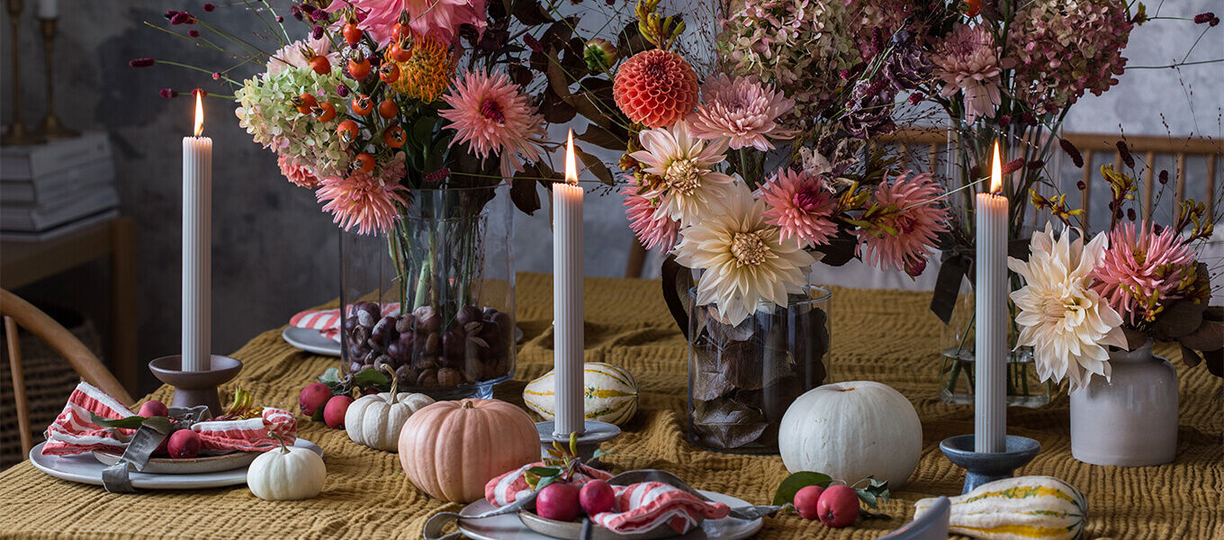 Nahaufnahme einer herbstlichen Tischdeko mit Dahlien, Kürbissen und Kerzen