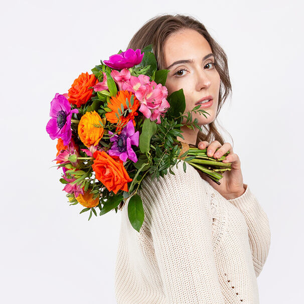 Junge Frau mit buntem Frühlingsstrauß aus Rosen, Anemonen und Gerbera – Inspiration zum Internationalen Frauentag