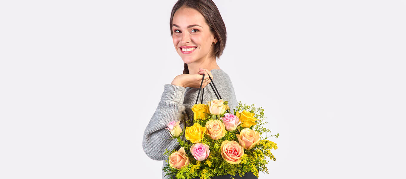 Lächelnde Frau hält einen farbenfrohen Blumenstrauß mit gelben, rosa und apricotfarbenen Rosen.