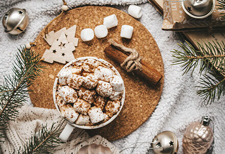 Tasse mit heißem Kakao und Marshmallows, dekoriert mit Zimt und winterlicher Weihnachtsdeko.