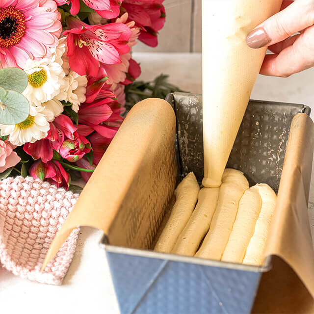 Herzkuchen Step 4 Heller Teig wird mit einem Spritzbeutel in eine Kastenform gespritzt, als untere Schicht für einen Überraschungskuchen.