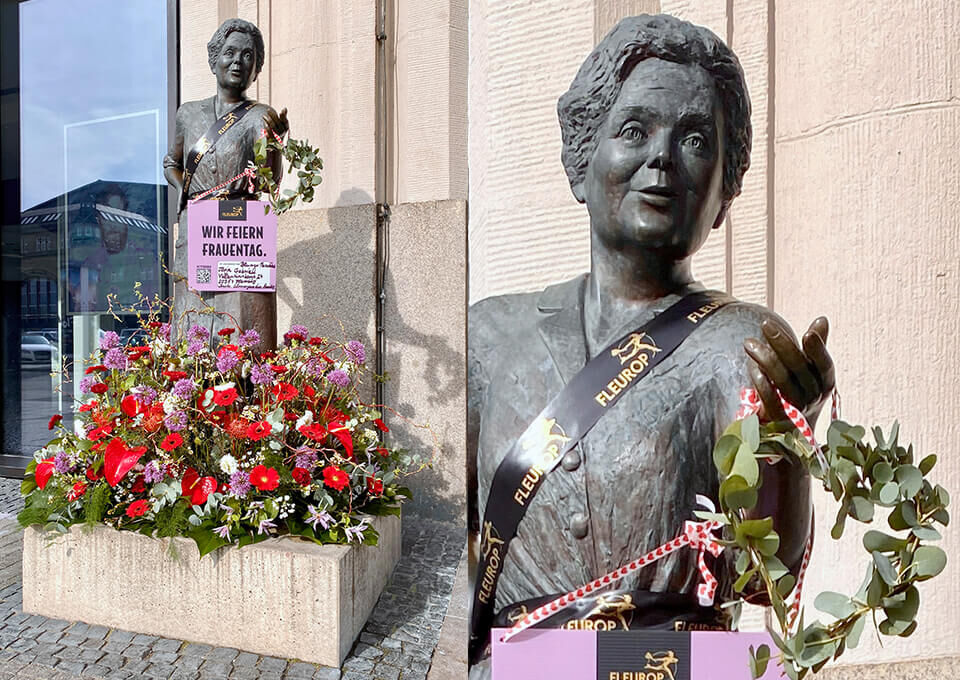 Bronzebüste von Heidi Kabel in Hamburg, mit roten und weißen Blumenarrangements sowie einem Blumenkranz zum Frauentag geschmückt.