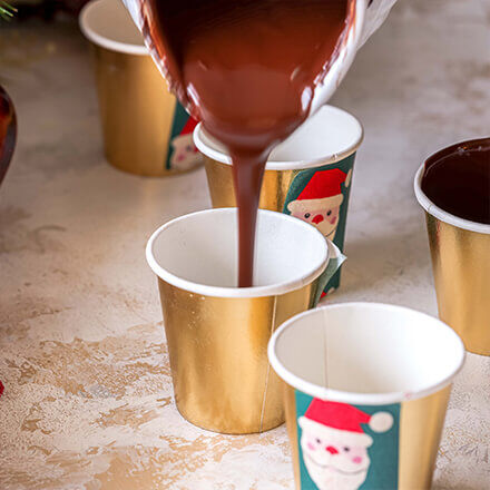 Goldene Papierbecher, in die flüssige Schokolade gegossen wird, als Basis für die Hot Chocolate Bomb Cups.