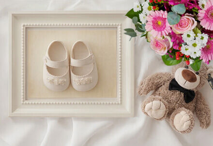 Geschenk zur Geburt mit Babyschuhen im Bilderrahmen und buntem Blumenstrauß