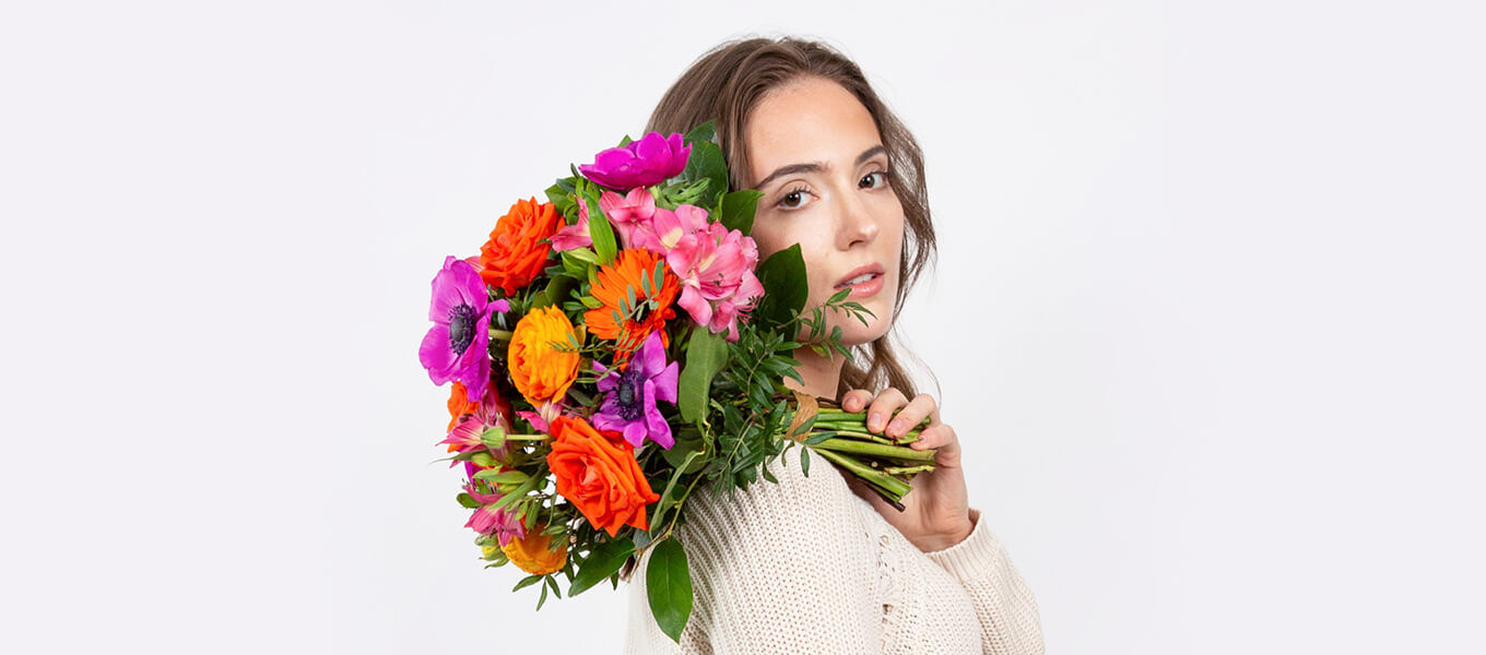Frau hält farbenfrohen Blumenstrauß in Pink, Orange und Violett – Motiv für Frauentag Sprüche und Blumengrüße