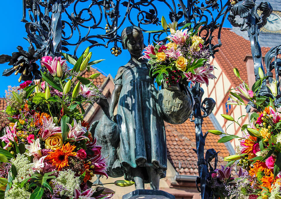 Bronzefigur des Gänseliesels in Göttingen, reich verziert mit bunten Lilien, Rosen und Gerbera anlässlich des Frauentags.