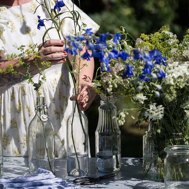 Tischdeko für Gartenparty - Step 4 Die Frau beginnt, blaue Ritterspornblüten in die mit Wasser gefüllten Flaschen zu arrangieren.