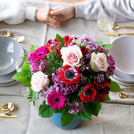 Eine prachtvoller Blumenstrauß in Rosa-Pink-Rot steht auf einem Tisch.
