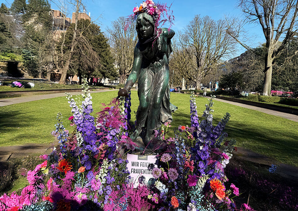 Kugelspielerin in Düsseldorf mit Blumen geschmückt zum Frauentag Bronzestatue der Kugelspielerin in Düsseldorf, festlich mit bunten Blüten in Lila, Pink und Orange dekoriert zum Internationalen Frauentag.