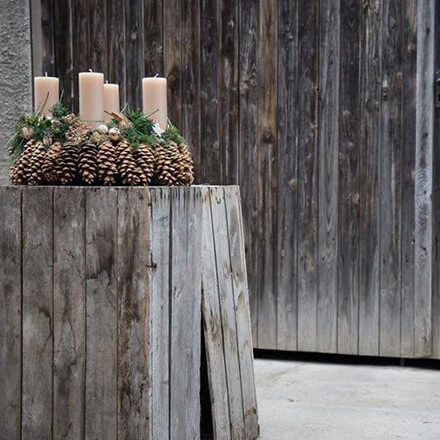Ein Adventskranz aus Kiefernzapfen steht in einer Holzscheune.
