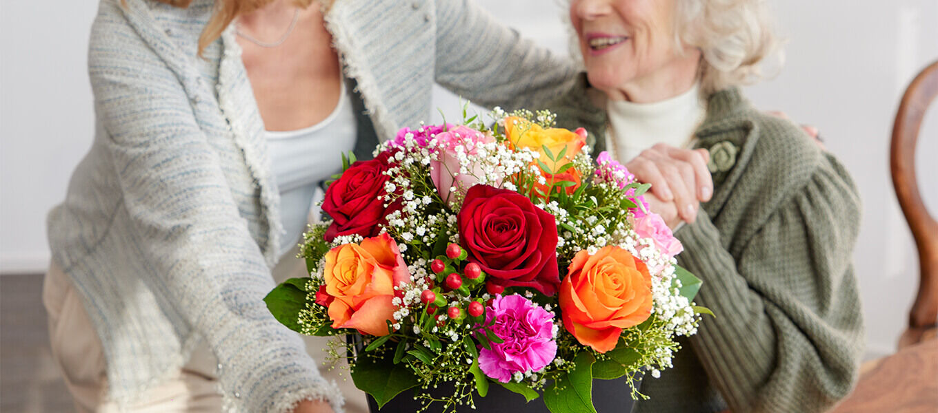 Tochter überreicht ihrer Mutter zum 80. Geburtstag einen bunten Blumenstrauß von Fleurop als liebevolles Geschenk.