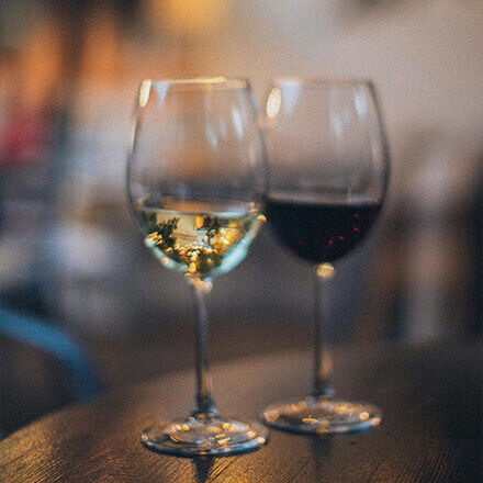  Zwei elegante Weingläser, eines mit Rotwein und das andere mit Weißwein, auf einem hölzernen Tisch in einer gemütlichen Atmosphäre.